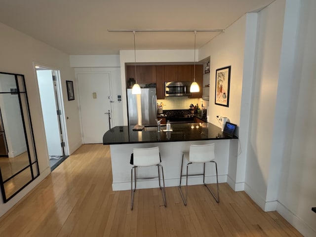 kitchen featuring light hardwood / wood-style flooring, a breakfast bar, stainless steel appliances, tasteful backsplash, and kitchen peninsula