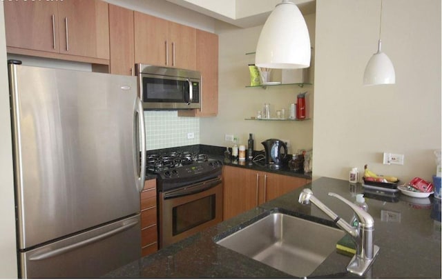 kitchen with appliances with stainless steel finishes, sink, backsplash, dark stone counters, and hanging light fixtures