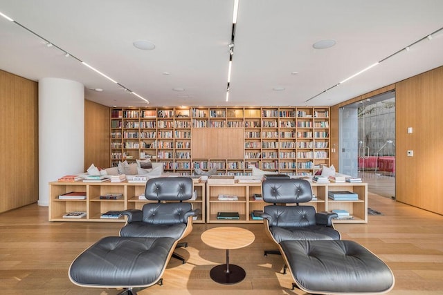 living area featuring built in features, wood finished floors, wood walls, track lighting, and wall of books