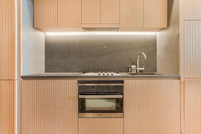 kitchen with oven, a sink, gas cooktop, cream cabinets, and decorative backsplash