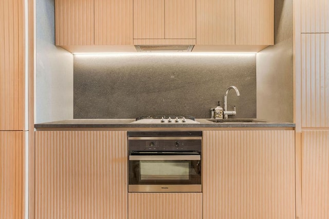 kitchen with gas stovetop, decorative backsplash, light brown cabinets, a sink, and oven