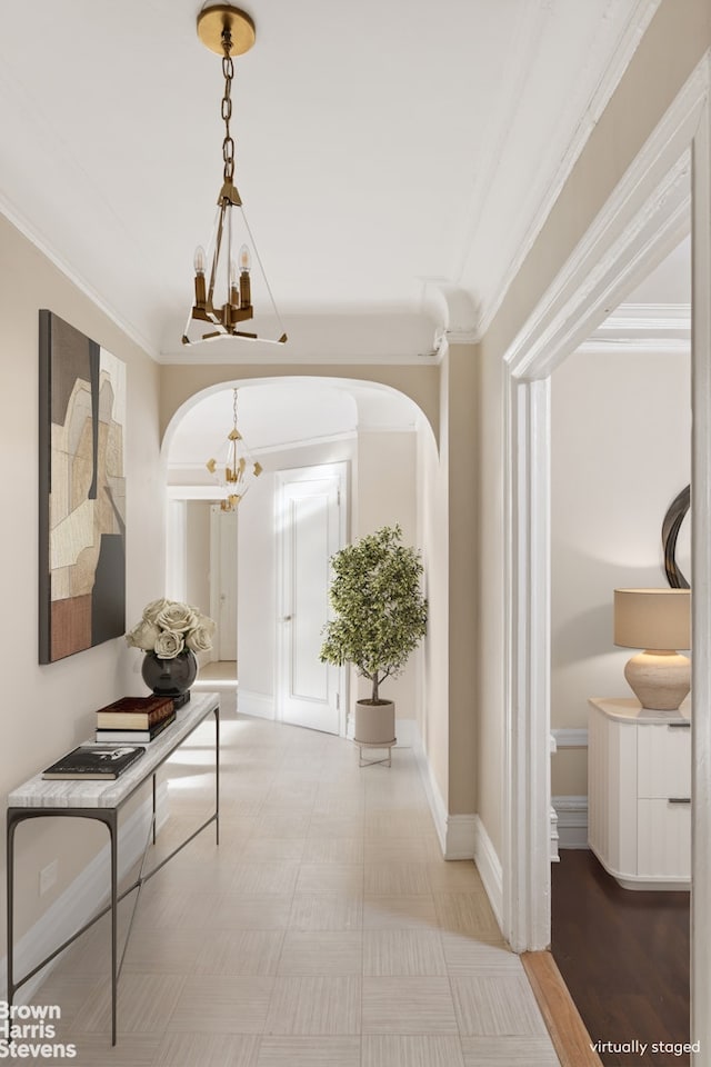 hall with baseboards, ornamental molding, arched walkways, and a notable chandelier