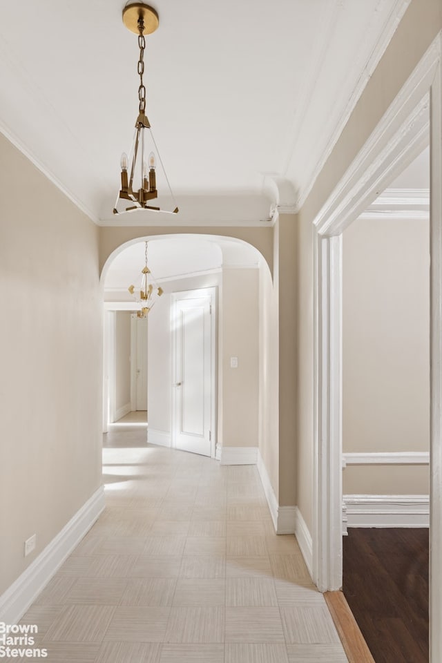 hallway with arched walkways, crown molding, baseboards, and an inviting chandelier