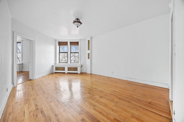 spare room featuring radiator, light wood-style flooring, and baseboards