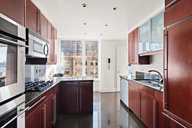 kitchen with stainless steel appliances, granite finish floor, a sink, baseboards, and glass insert cabinets