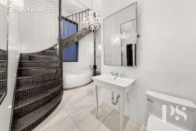 71-73 Bleecker St Unit 2E, New York City, NY 10012 - bathroom featuring a chandelier, a freestanding bath, toilet, tile walls, and tile patterned flooring