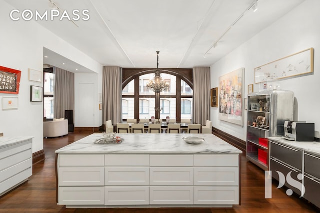 71-73 Bleecker St Unit 2E, New York City, NY 10012 - kitchen with a chandelier, track lighting, dark wood-style flooring, white cabinets, and light stone countertops