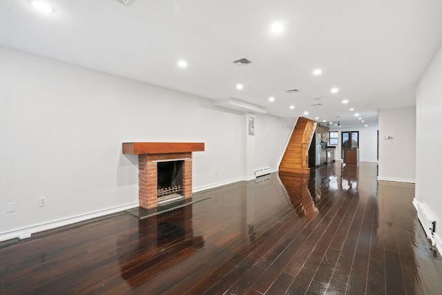 unfurnished living room with dark wood-type flooring, baseboard heating, and a brick fireplace