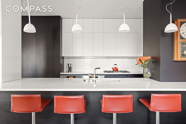 kitchen with a breakfast bar area, a sink, white cabinetry, modern cabinets, and decorative light fixtures