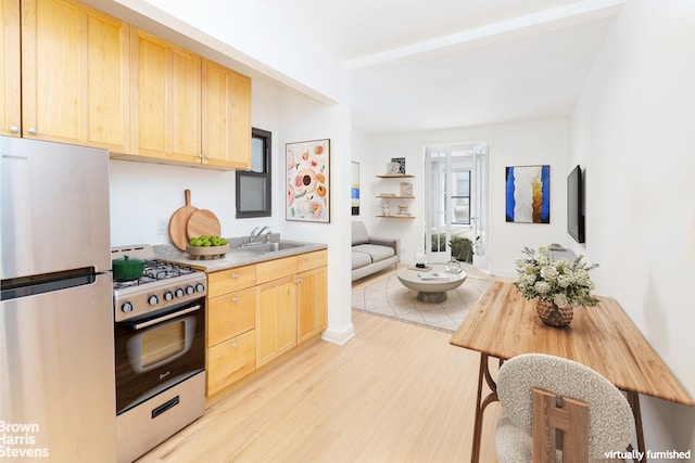 kitchen featuring range with gas cooktop, light wood finished floors, freestanding refrigerator, light brown cabinets, and a sink