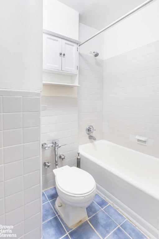 bathroom with tile patterned floors, tile walls, toilet, and tiled shower / bath combo