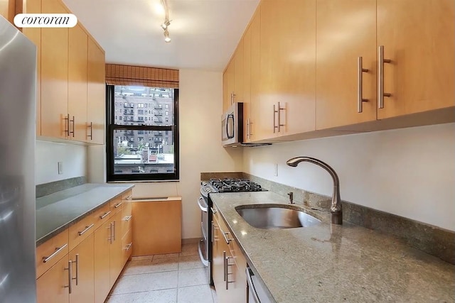 kitchen with light brown cabinetry, a sink, stone countertops, appliances with stainless steel finishes, and light tile patterned flooring