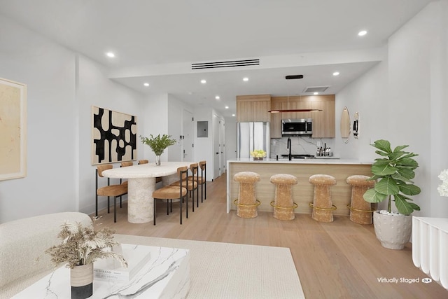 kitchen featuring backsplash, electric panel, light brown cabinetry, kitchen peninsula, and light wood-type flooring