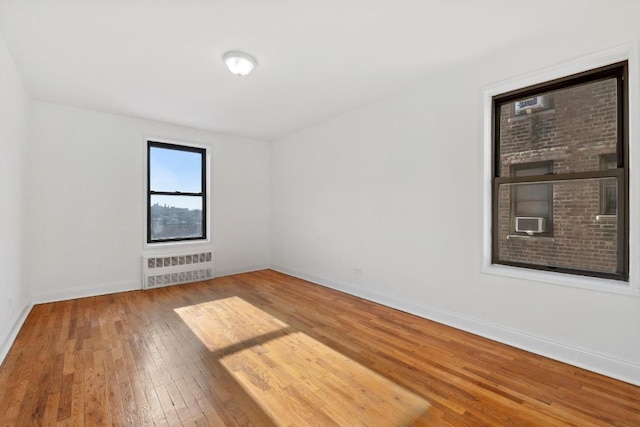 empty room featuring hardwood / wood-style flooring, cooling unit, and radiator heating unit