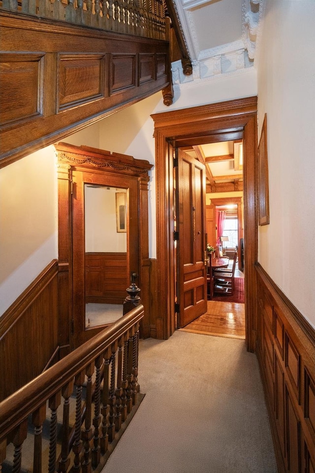 corridor featuring wood walls, light colored carpet, and wainscoting