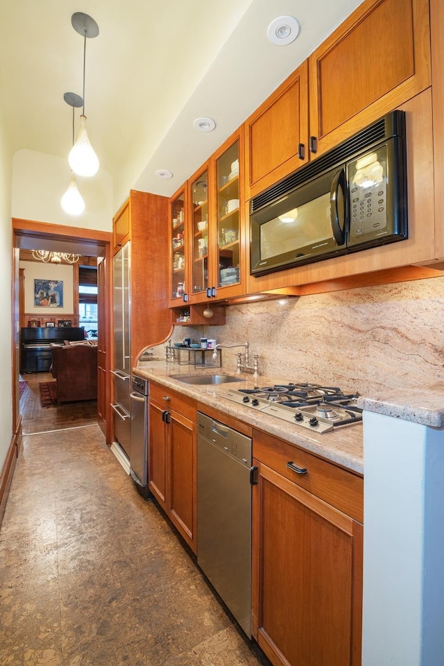 kitchen featuring stainless steel appliances, a sink, brown cabinetry, glass insert cabinets, and decorative light fixtures