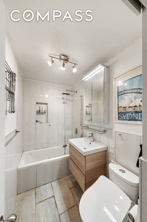 full bathroom with toilet, tile walls, tiled shower / bath combo, and vanity