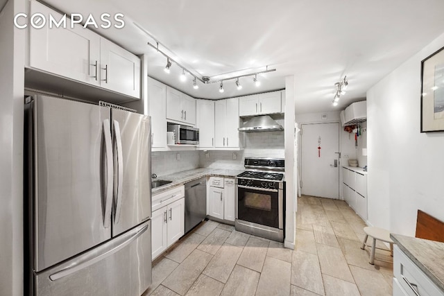 kitchen featuring appliances with stainless steel finishes, track lighting, tasteful backsplash, light stone countertops, and white cabinets