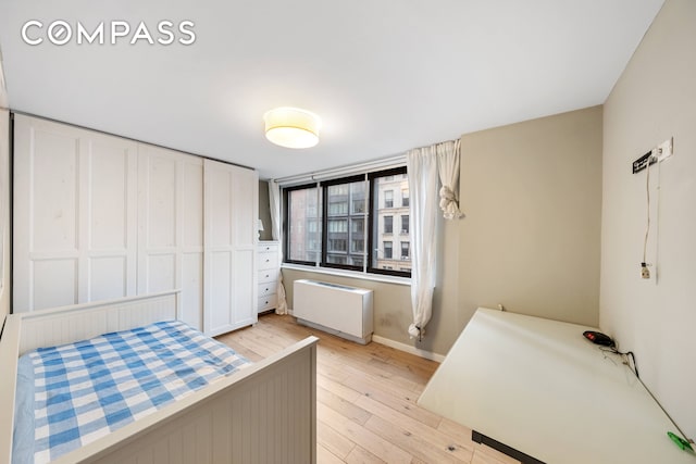 bedroom featuring radiator heating unit, light wood finished floors, and baseboards