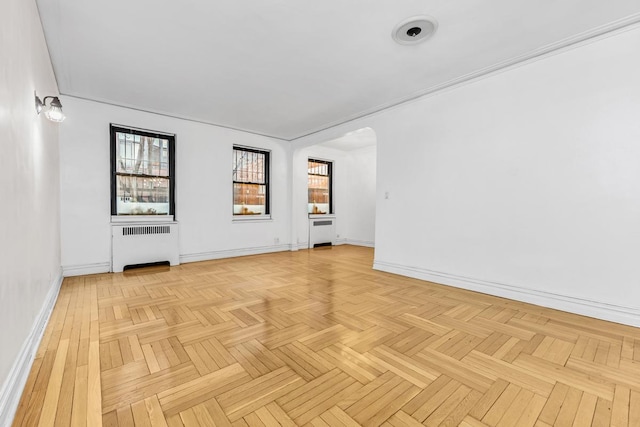 empty room with arched walkways, radiator heating unit, and baseboards