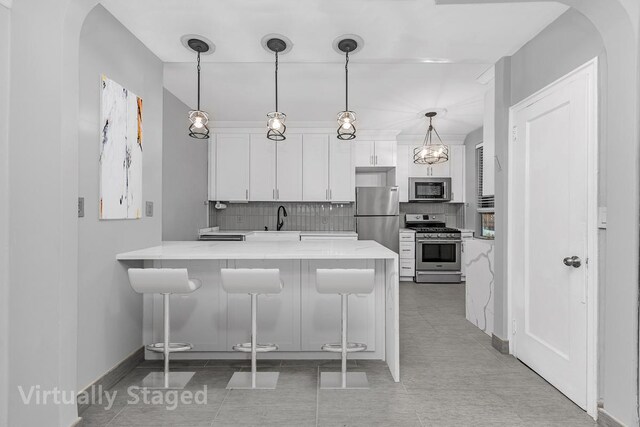 kitchen with white cabinets, a kitchen breakfast bar, a peninsula, stainless steel appliances, and pendant lighting