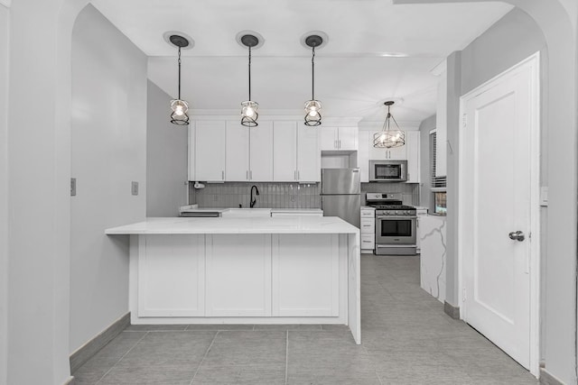 kitchen with white cabinets, appliances with stainless steel finishes, a peninsula, pendant lighting, and a sink