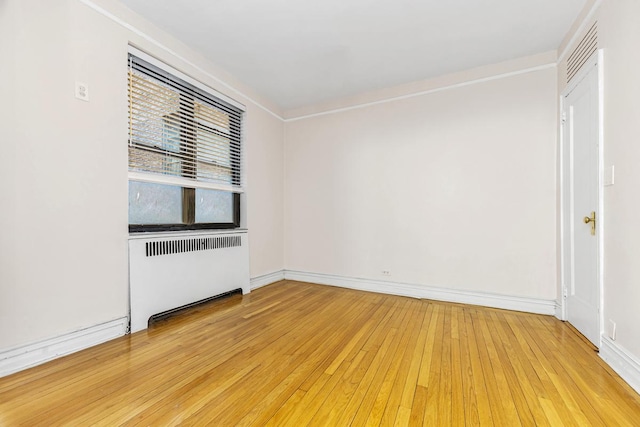 empty room featuring baseboards, light wood-style floors, and radiator