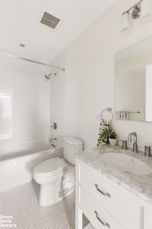 full bathroom with tiled shower / bath, tile patterned floors, vanity, tile walls, and toilet