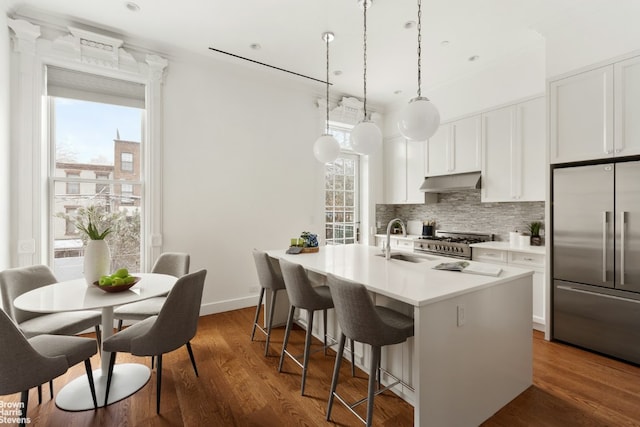 kitchen with pendant lighting, a center island with sink, sink, white cabinets, and high quality appliances