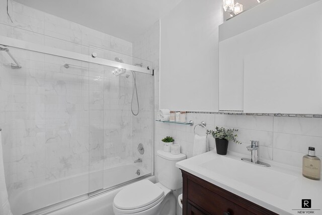 full bathroom with toilet, bath / shower combo with glass door, tile walls, vanity, and decorative backsplash