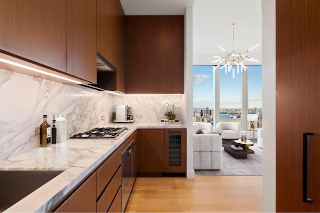 kitchen with wine cooler, stainless steel gas stovetop, decorative backsplash, a chandelier, and light wood-type flooring