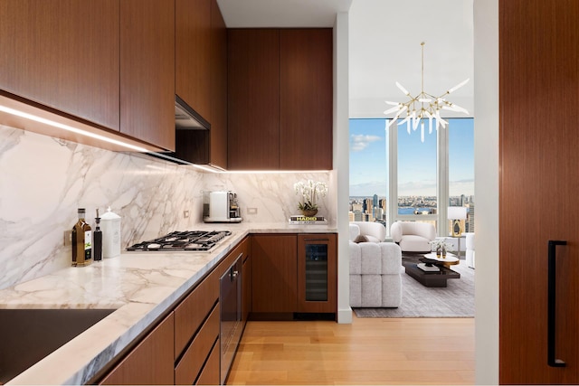 kitchen with light stone countertops, stainless steel gas stovetop, wine cooler, light wood-style floors, and tasteful backsplash