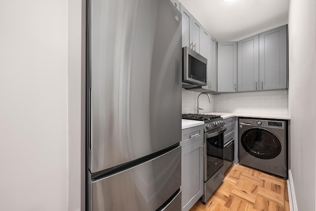 kitchen with stainless steel appliances, light countertops, gray cabinets, tasteful backsplash, and washer / dryer