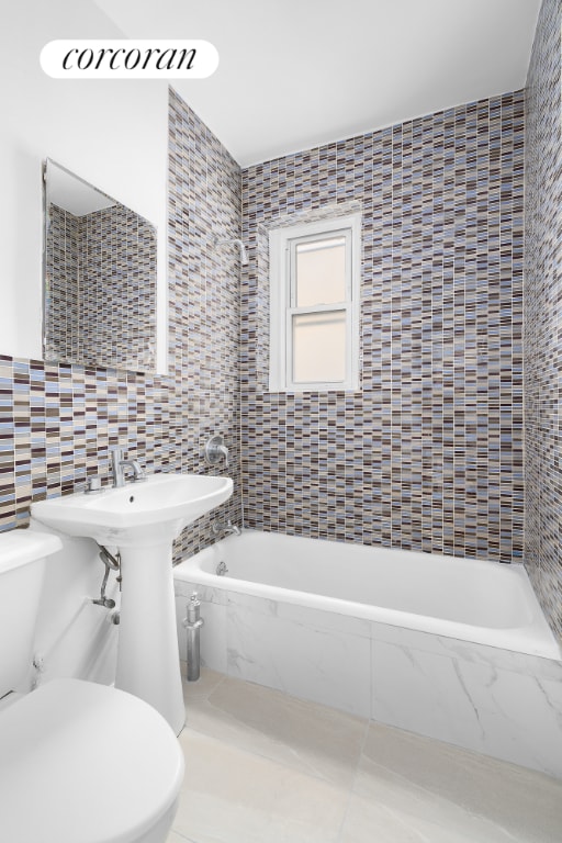 bathroom with a relaxing tiled tub, tile walls, toilet, and tile patterned flooring