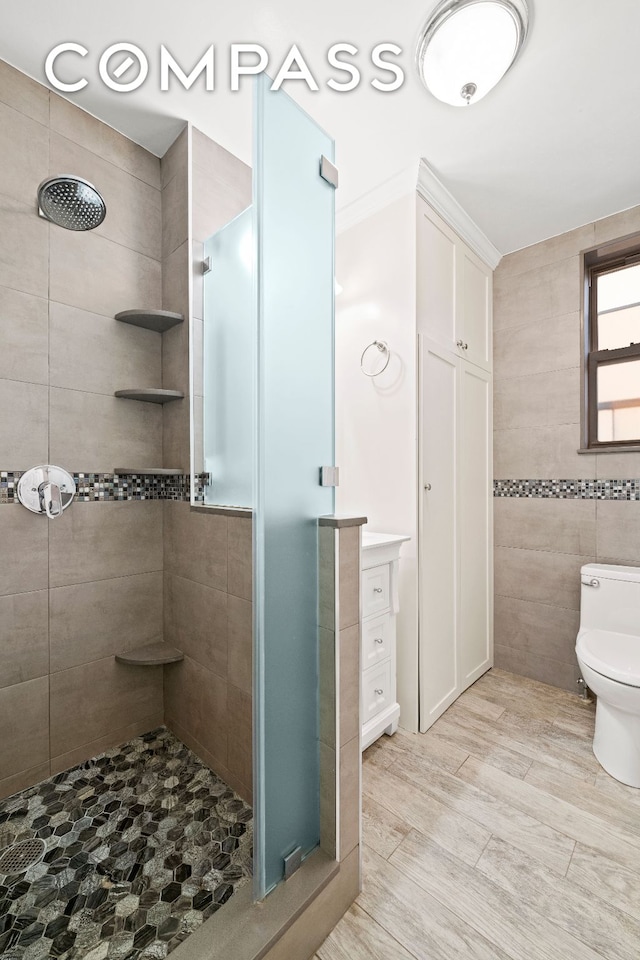 bathroom with toilet, a shower stall, tile walls, and wood finished floors