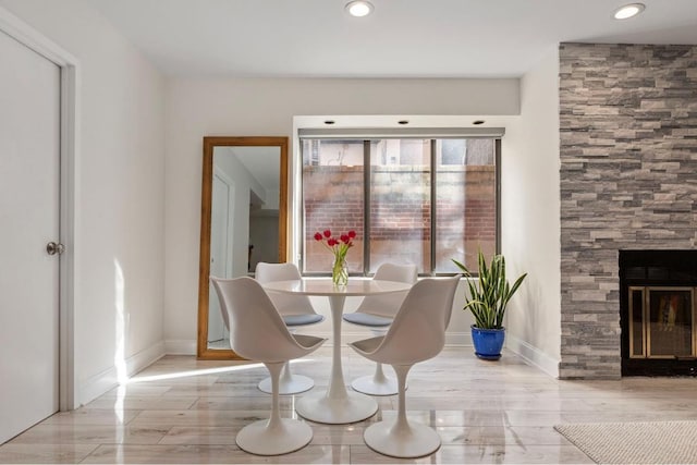 dining room featuring light wood-type flooring and a stone fireplace