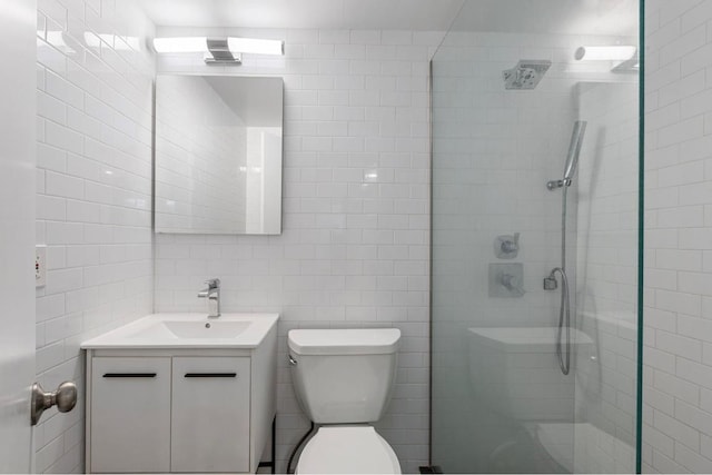 bathroom with tile walls, toilet, a shower with door, and vanity