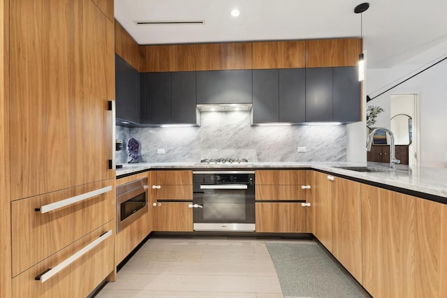 kitchen featuring wall oven, stainless steel microwave, backsplash, pendant lighting, and sink