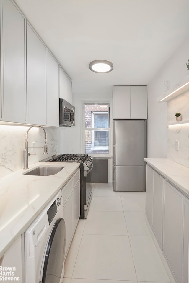 kitchen featuring stainless steel appliances, washer / dryer, white cabinetry, and a sink