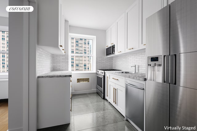 kitchen with backsplash, light stone counters, stainless steel appliances, white cabinetry, and a sink