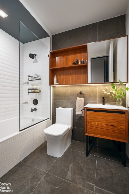 full bathroom featuring tile walls, tiled shower / bath combo, vanity, toilet, and tile patterned floors