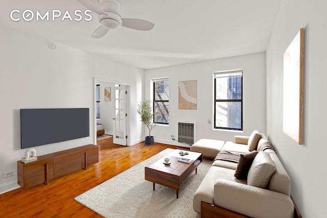 living room featuring a ceiling fan, visible vents, baseboards, and wood finished floors