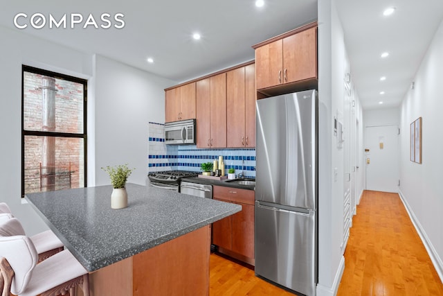 kitchen with light wood finished floors, tasteful backsplash, dark countertops, appliances with stainless steel finishes, and a center island