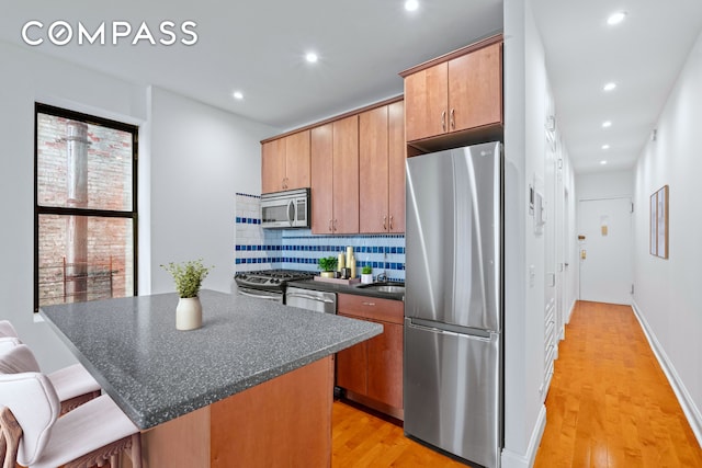 kitchen featuring appliances with stainless steel finishes, dark countertops, decorative backsplash, light wood-type flooring, and a kitchen island