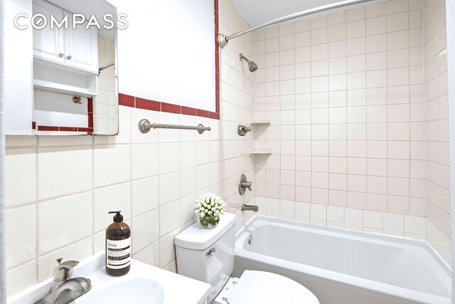 bathroom featuring tile walls, a sink, shower / tub combination, and toilet
