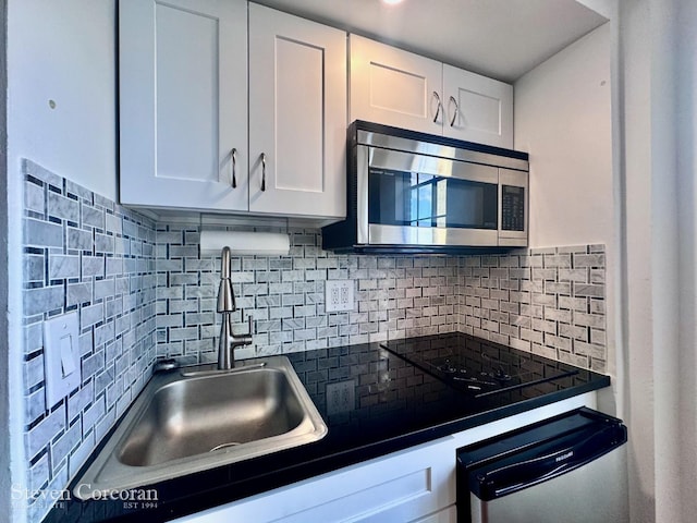 kitchen with stainless steel appliances, dark countertops, backsplash, white cabinetry, and a sink