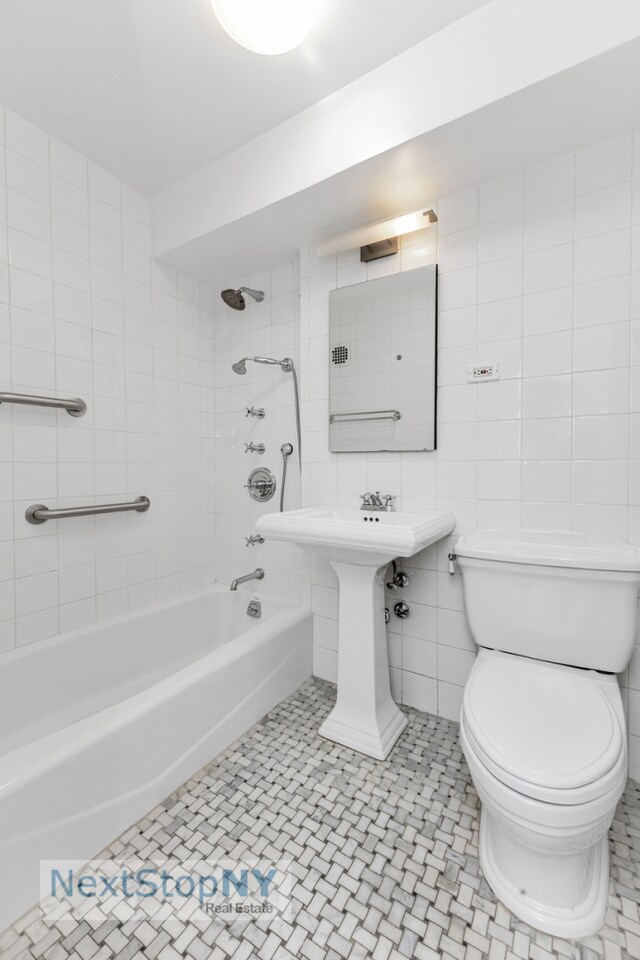 bathroom featuring tile patterned flooring, tiled shower / bath, tile walls, and toilet