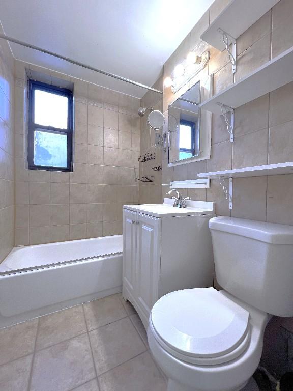 full bathroom with tile walls, tile patterned flooring, vanity, tiled shower / bath, and toilet