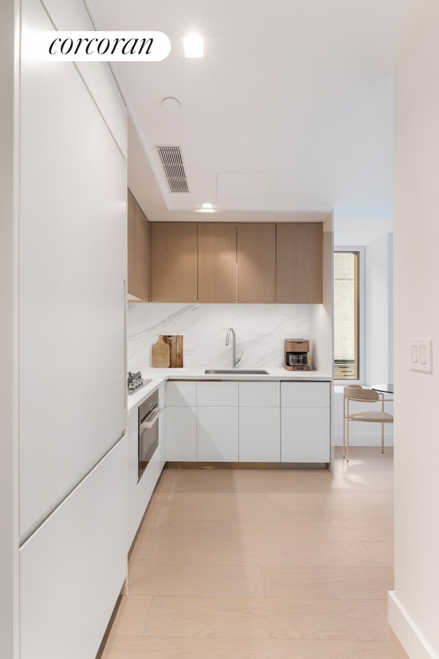 kitchen with tasteful backsplash, light hardwood / wood-style floors, sink, white cabinetry, and stainless steel appliances