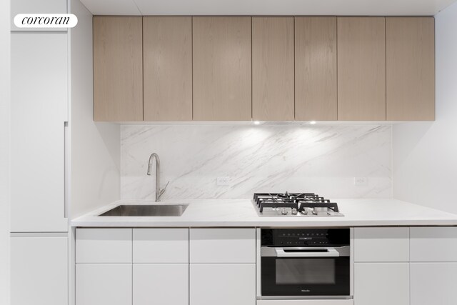 kitchen featuring stainless steel gas cooktop, a sink, oven, light countertops, and modern cabinets